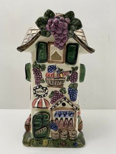 a ceramic figurine that has grapes on the roof and in front of a house