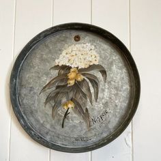 a metal plate with flowers painted on the front and back of it, hanging on a wall