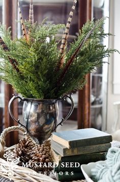 a vase filled with lots of green plants and pine cones on top of a table