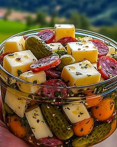 a hand holding a glass bowl filled with pickles and cheese