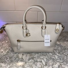 This Nwt Coach Cara Satchel In Soft Pebbled Leather In Chalk White Color Is A Versatile Piece For Any Occasion. It Is Medium Sized With A 10 1/2" Bag Width, 5 1/2" Bag Depth, And 7 1/2" Bag Height. The Bag Has Double Handles And A Detachable Cross-Body Strap For A Variety Of Carrying Options. It Is Lined With Polyester And Has Inner Pockets For Storing Your Essentials. The Hardware Is Antique Brass And The Bag Has A Zipper Closure. The Satchel Also Comes With A Brand Card, A Detachable Strap, A White Pebbled Leather Top Handle Bag, Luxury White Pebbled Leather Bag, White Pebbled Leather Shoulder Bag With Detachable Strap, White Rectangular Pebbled Leather Shoulder Bag, White Pebbled Leather Shoulder Bag With Top Handle, Chic White Pebbled Leather Bag, Elegant White Pebbled Leather Bag, White Pebbled Leather Shoulder Bag For Travel, White Pebbled Leather Bag With Gold-tone Hardware