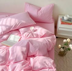 a bed with pink sheets and pillows on top of it next to a vase filled with flowers