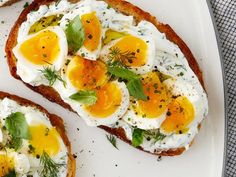 two pieces of toast with eggs and herbs on them