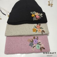 three beanies with flowers on them sitting next to each other in front of a white table