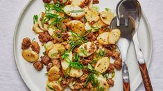 a white plate topped with meat and veggies next to a silver spoon on top of a table