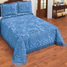 a bed with blue bedspread and pillows on top of wooden floors in a room