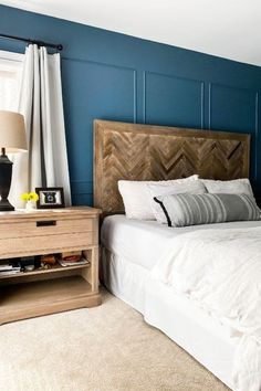 a bedroom with blue walls, white bedding and a nightstand in front of the bed