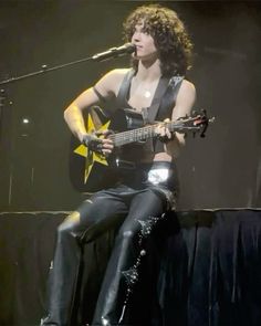 a woman sitting on top of a stage with a guitar in her hand and singing into a microphone