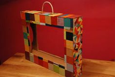 a colorful wooden frame sitting on top of a wooden table next to a red wall