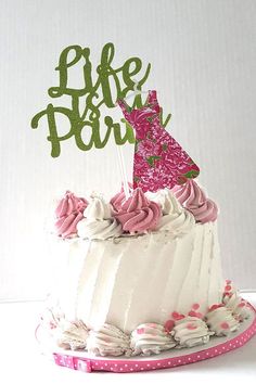 a white cake with pink frosting and a green life is party topper