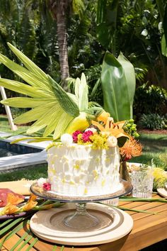 a white cake sitting on top of a wooden table next to flowers and greenery