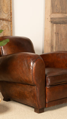 a brown leather chair sitting in front of a wooden paneled door with a potted plant