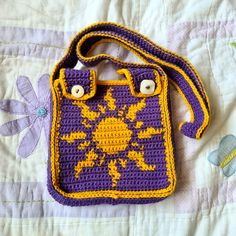 a crocheted purple and yellow purse sitting on top of a white quilted bed