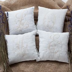 four white embroidered pillows sitting on top of a couch next to some lavenders and grass