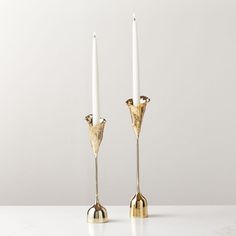 two gold candlesticks sitting next to each other on a white counter top with one candle in the middle