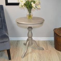 a small table with flowers in a vase on it next to a chair and basket