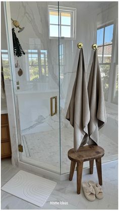 two towels are hanging on the glass shower door in this white bathroom with wooden stool