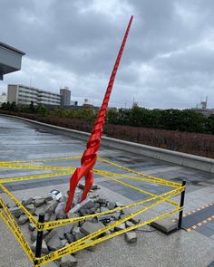 a large red sculpture sitting in the middle of a parking lot next to yellow caution tape