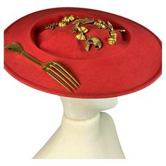 Circa 1980 France A stunning scarlet wool felt Hat Capeline with Surrealist inspiration by French designer Isabel Canovas dating from the 1980s. Entitled déjeuner au Stresa (lunch in Stresa), this capeline is shaped like an oval plate filled with various charms and a gilded bronze fork on one edge! A wide black elastic band and headband behind the bun or the nape of the neck reveals the Isabelle Canovas label. Very slight creasing of the base plate resting on the skull, otherwise no other defect 1980’s Fashion, Thrift Flips, Oval Plate, Antique Hats, French Designer, Red Felt, The 1980s, Felt Hat, French Design