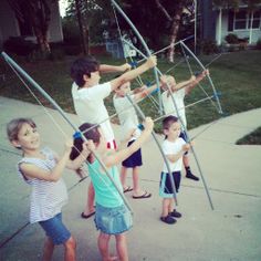 four children playing with kites on the sidewalk in front of a house and one child is holding two poles