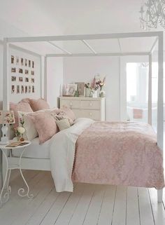 a white bedroom with pink bedding and decor on the walls, along with a chandelier