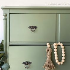 a green dresser with wooden beads and rings on the drawer knobs next to it