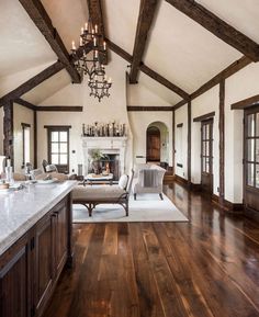 a large open living room with wood floors and white walls, chandelier hanging from the ceiling