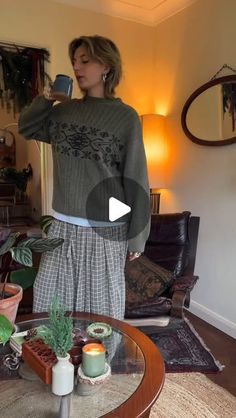 a woman is taking a selfie in her living room while wearing a sweater and skirt