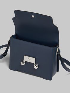 Trunkaroo medium rectangular shoulder bag crafted from calfskin leather. Front flap with magnetic closure, featuring engraved Marni lettering and oversized stud details. Contoured base on the front and back. One compartment with inside pocket. Lined in nappa leather. Detachable and adjustable buckled shoulder strap: can also be worn as a clutch. Designer Rectangular Flap Bag With Metal Hardware, Designer Satchel Saddle Bag With Palladium Hardware, Designer Saddle Satchel Bag With Palladium Hardware, Designer Rectangular Box Bag With Metal Hardware, Designer Leather Box Bag With Palladium Hardware, Designer Saddle Shoulder Bag With Palladium Hardware, Designer Satchel Flap Bag With Palladium Hardware, Modern Rectangular Saddle Bag With Branded Hardware, Designer Box Bag With Silver-tone Hardware For Travel