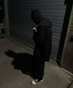 a person standing in front of a garage door looking at their cell phone while wearing a hoodie