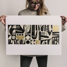 a woman holding up a black and white art print with geometric shapes on it's sides