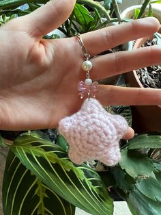 a hand holding a pink crochet heart shaped keychain in front of a potted plant