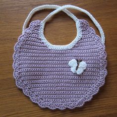 a crocheted bag with a white flower on the front and purple bottom, sitting on a wooden surface