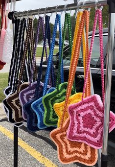 colorful crocheted bags hanging from a rack in a parking lot next to a car