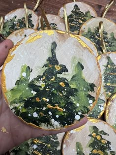 a hand holding a plate with painted christmas trees on it and gold trimmings