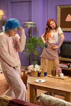 two women in pajamas are standing near a coffee table and television set with blue hair