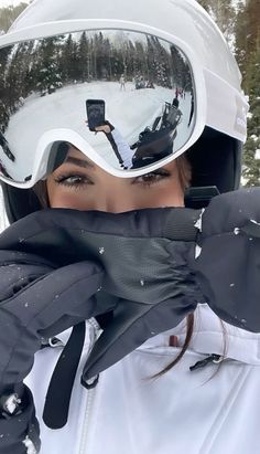 a woman wearing ski goggles and holding her face up to the camera while standing in the snow