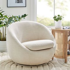 a white chair sitting on top of a rug next to a table and potted plant