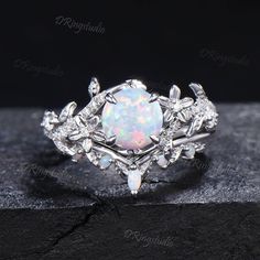 a white opal and diamond ring on top of a black stone slab with the words,