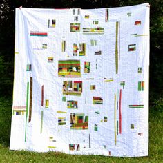 a large white quilt hanging on the side of a grass covered field with trees in the background