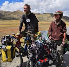 two people standing next to their bikes in the mountains