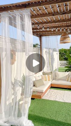 an outdoor living area with couches and curtains on the roof, covered in grass