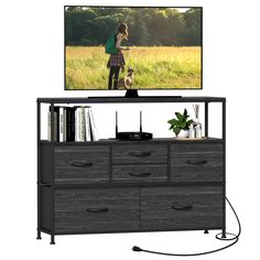 a woman standing in front of a flat screen tv on top of a wooden dresser