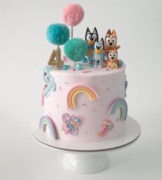 there is a cake decorated with animals and rainbows on the top, along with pom poms