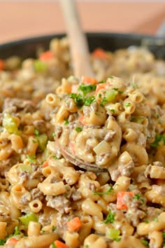 macaroni and cheese is being stirred with a wooden spoon in a skillet