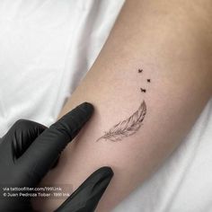 a small feather tattoo on the right inner arm and leg, with tiny black dots coming out of it