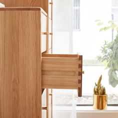 a wooden cabinet next to a potted plant in front of a window with an open door