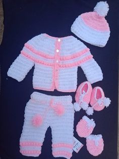 a crocheted baby outfit and booties is displayed on a black blanket with pink trim