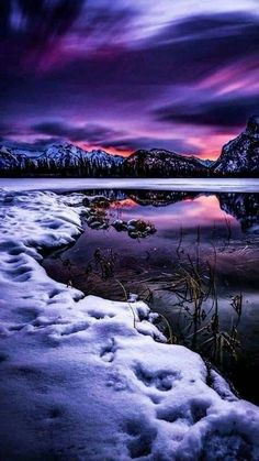 the sun is setting over a lake with snow on it and mountains in the background