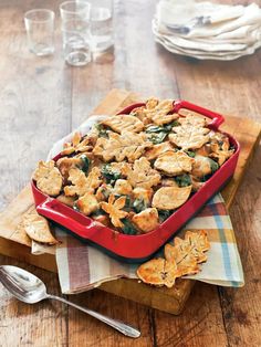 a red casserole dish filled with spinach, cheese and crackers on a wooden table